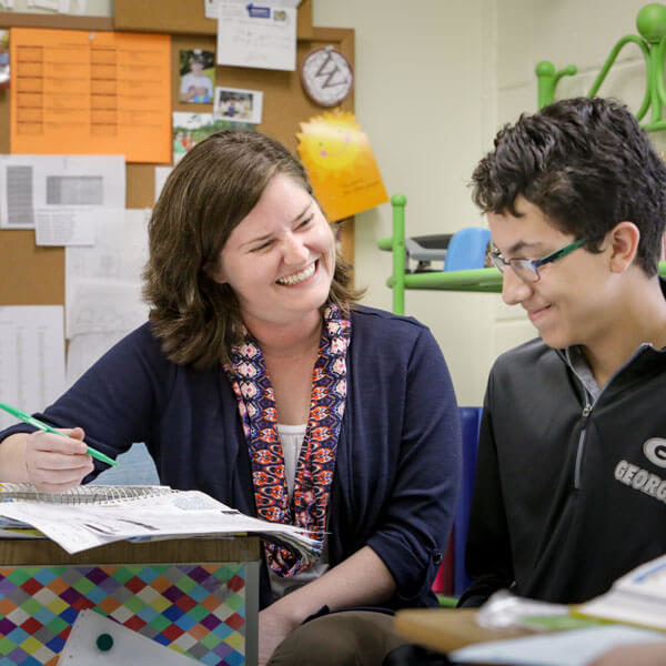 female teacher smiles while helping young male student with schoolwork